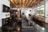 Modern loft-style apartment featuring a sleek open-concept living area with polished concrete floors, industrial beams, and large windows for natural light. Cozy seating area with plush gray sofa and entertainment nook with game machine.
