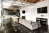 Modern open-concept living space featuring industrial-style kitchen with rustic accents, cozy gray sofa, and sleek furnishings.
