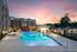 Luxurious apartment complex featuring a stunning illuminated poolside area, surrounded by modern architecture at sunset.