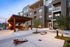 Modern apartment complex exterior with inviting outdoor seating area under a stylish wooden pergola, surrounded by lush greenery and playful cornhole setup, perfect for entertaining.