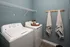 Modern laundry room featuring top-loading washer and dryer with stylish wall hooks and decorative accents in a serene blue setting.