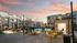 Charming apartment complex with a sunset backdrop, featuring a sparkling pool, cozy patio with string lights, and modern outdoor seating area.