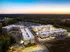 Aerial view of a modern apartment complex at sunset, showcasing well-lit buildings with a central courtyard and surrounding lush greenery.