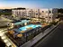 Modern apartment complex at sunset with sparkling illuminated pool, surrounded by stylish lounge chairs and vibrant umbrellas, offering luxurious outdoor living.
