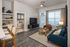 Modern living room with stylish furnishings, featuring a large window, cozy seating, and decorative shelving. Open doorway leads to a beautifully appointed bedroom.