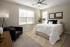 Inviting bedroom with a plush white comforter, elegant decor, and ample natural light streaming through large windows.