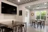 Modern communal space featuring sleek metal tables, stylish black stools, and a patterned ceiling, enhanced by natural light from large windows.