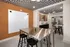 Modern communal space with sleek stainless steel tables, stylish black stools, vibrant decor, and geometric ceiling design.