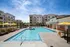 Luxurious apartment complex featuring a sparkling outdoor pool with yellow sun umbrellas and comfortable lounge chairs under a clear blue sky.