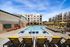 Luxurious apartment complex featuring a sparkling swimming pool, surrounded by stylish lounge chairs and vibrant yellow umbrellas, offering resort-style living.