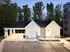 Charming modern garage with sleek white siding and pitched roof, nestled amid lush greenery and adjacent to a stylish apartment building.