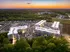 Stunning aerial view of modern apartment complex surrounded by lush greenery at sunset, featuring pristine architecture and ample parking.