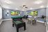 Vibrant recreation room featuring a pool table, foosball table, and modern seating area with art-adorned walls and dual computer desks.
