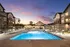 Luxurious apartment complex with illuminated poolside, elegant lounge chairs, and stylish architecture at sunset.