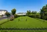 Lush green dog park featuring agility equipment and benches, surrounded by modern apartment buildings and vibrant trees.