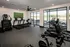 Modern fitness center with sleek exercise equipment, large windows, and a wall-mounted TV, offering natural light and vibrant workout vibes.