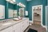 Inviting bathroom with teal walls, double sink vanity, elegant lighting, and a spacious walk-in closet.