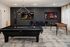 Modern entertainment room featuring a sleek black pool table, foosball table, and dual wall-mounted TVs displaying sports.