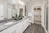 Luxurious bathroom featuring dual sinks with granite countertop, elegant framed artwork, and a spacious walk-in closet with ample shelving.