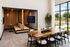 Modern communal workspace featuring a cozy booth seating area and a large wooden conference table, bathed in natural light from expansive windows.
