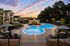 Luxurious apartment complex featuring a large, beautifully lit swimming pool with elegant lounge areas and scenic sunset views.