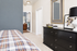 Charming bedroom with sleek black dresser, modern decor, and a cozy plaid bedspread offering a glimpse into a stylish en-suite bathroom.
