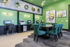 Modern office space with vibrant green walls, featuring a computer workstation and stylish seating area with patterned chairs and abstract art.