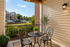 Charming outdoor patio with elegant wrought iron table and chairs, surrounded by lush greenery and illuminated by soft lighting, offering a serene view of a picturesque neighborhood.