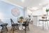 Chic dining area with a round table, modern black chairs, and an artful wall piece, adjacent to a sleek white kitchen with breakfast bar seating.