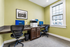 Bright modern office space featuring comfortable seating, dual computer stations, and a multi-function printer adjacent to a large window for natural light.