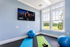 Bright home gym featuring large windows, a wall-mounted exercise video screen, yoga mats, a stability ball, and scenic outdoor views.