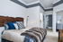 Inviting bedroom with a rustic wooden headboard, plush bedding, and elegant floor lamp, leading to a bright hallway and modern living space.