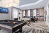 Luxurious apartment entertainment room featuring a sleek pool table, stylish foosball setup, and modern workspace with computers, perfect for leisure and productivity.