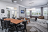 Modern community space featuring a sleek wooden dining table, comfortable seating, foosball table, and pool table with ample natural light from large windows.