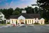 Charming community center with inviting white facade and beautiful landscaping, set against a backdrop of lush greenery and a stunning evening sky.