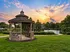 Charming gazebo set against a breathtaking sunset, overlooking a tranquil pond with lush greenery and serene surroundings.