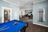 Contemporary recreation room featuring a vibrant blue pool table, modern seating area with computers, and a wall-mounted TV, designed for relaxation and entertainment.