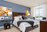 Elegant bedroom featuring a comfortable bed with stylish patterned bedding, accent pillows, and modern art. Room is beautifully lit by natural light from large windows and enhanced with sophisticated decor.