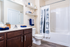 Bright and modern bathroom with elegant wood cabinets, sleek countertops, and a stylish shower curtain. Thoughtfully placed shelves add convenience and charm.