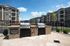 Inviting apartment complex featuring modern outdoor grills, perfect for entertaining. Surrounded by well-maintained landscaping and elegant facades under a sunny sky.