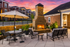 Charming outdoor patio with cozy fireplace, stylish seating, and umbrella-shaded table, set against a vibrant sunset sky and modern apartment backdrop.