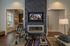 Luxurious living room with modern fireplace, textured wall, and sleek wooden flooring, offering a cozy yet stylish atmosphere. Open doorway reveals a chic kitchen with ambient lighting.