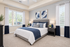 Elegant bedroom with modern decor, featuring a plush grey headboard, cozy blue accents, and large windows offering ample natural light.
