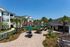 Charming apartment complex featuring lush landscaping, inviting patio area with green umbrellas, and a serene pond view.