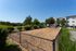 Charming apartment exterior with manicured landscaping, fenced grassy area, and sunny blue skies.