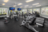 Modern fitness center with state-of-the-art equipment, including treadmills and exercise bikes, illuminated by natural light and multiple TV screens.
