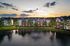 Charming apartment complex overlooking a tranquil pond with a picturesque fountain at sunset, surrounded by lush greenery.