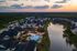 Stunning aerial view of a serene apartment complex featuring modern buildings, a sparkling pool, and a tranquil lake at sunset.