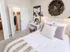 Chic bedroom with plush white bedding, cozy pillows, and modern decor, featuring an artistic wall piece and sleek workspace.
