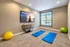 Bright yoga room with two blue mats, a screen displaying yoga options, and a serene view through large windows, perfect for home wellness.